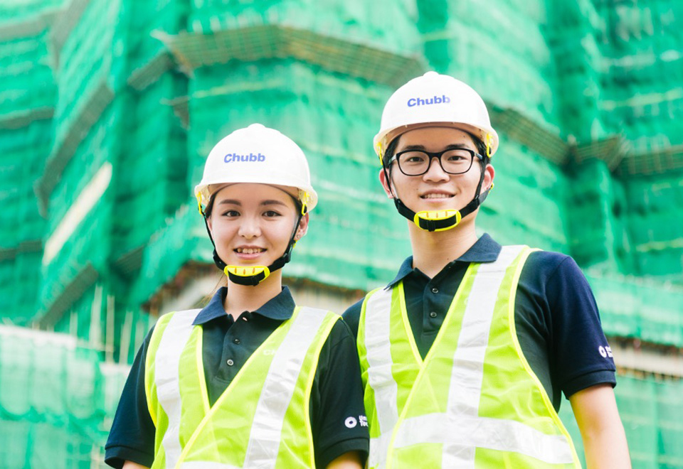 Two Chubb coworkers wear hard hats and yellow safety vests on a job site.