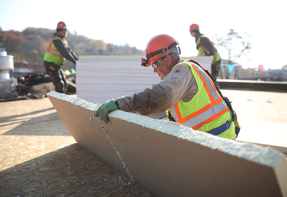 Three coworkers cut or carry insulation on a job site.