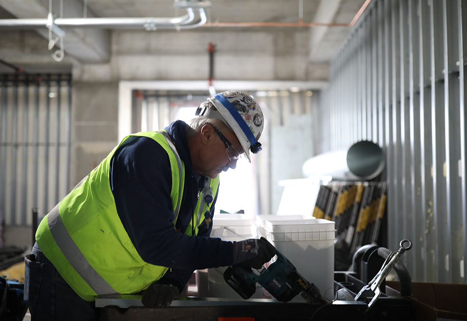 A coworker wearing safety gear drills on a job site.