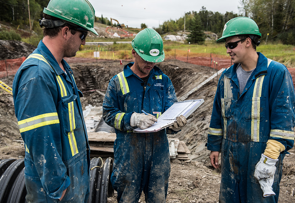 Three coworkers at Summit Pipeline Services discuss progress on a job site.