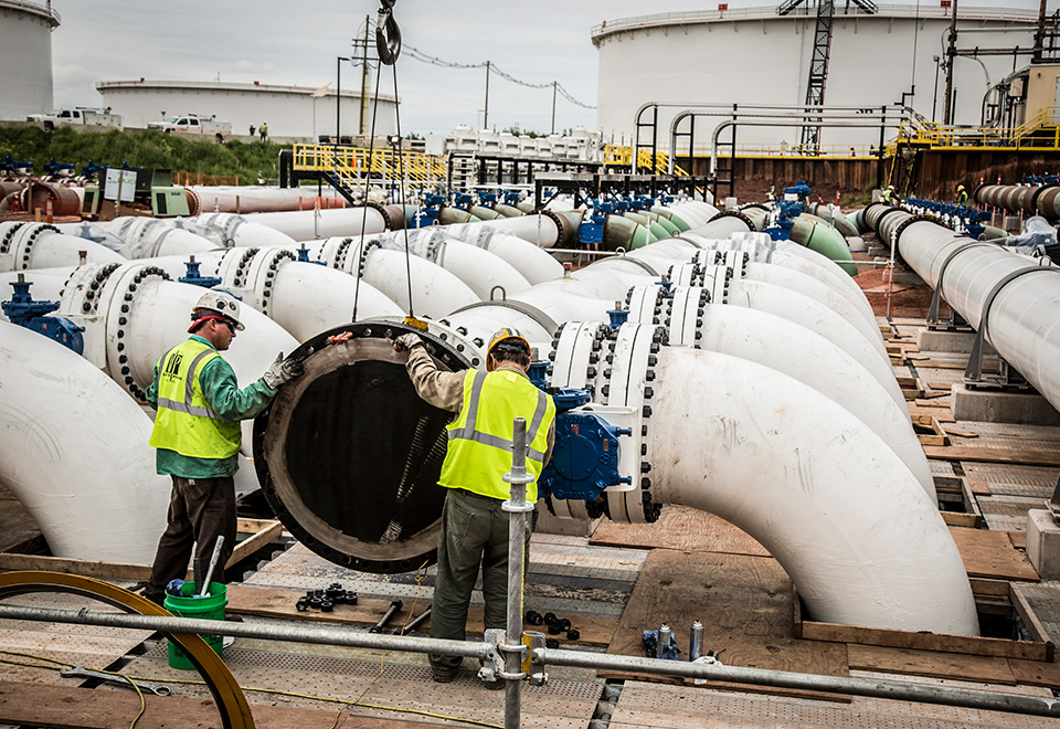 Two coworkers wearing safety gear work at a pipeline facility construction site.